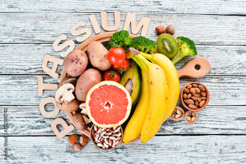 Foods containing natural potassium. K: Potatoes, mushrooms, banana, tomatoes, nuts, beans, broccoli, avocados. Top view. On a white wooden background. photo