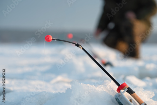 Winter fishing. Focus on the fishing rod. Fisherman sitting in the background