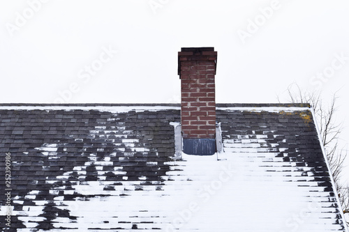 Wallpaper Mural Brown brick chimney on grey asphalt shingles roof partly covered with snow in winter against sky with copy space for text. Torontodigital.ca