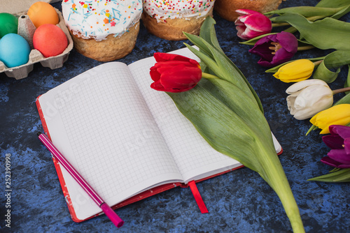 Fototapeta Naklejka Na Ścianę i Meble -  Easter.Notebook for writing,colorful eggs,spring tulips,cakes  on blue background.Holiday set.Happy religious day,traditional for people. Top view.Copy space.Concept