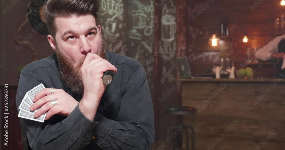 Man smoking and socializing while playing cards. Young man with a big beard in a pub with his friends. Playing cards and having fun. Man smoking and socializing while playing cards. Young man with a big beard in a pub with his friends. Playing cards and having fun.