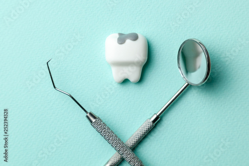 White tooth with caries on green mint background  and dentist tools mirror, hook. © adragan