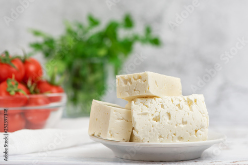 Large pieces of feta cheese in white plate and cherry tomatoes on light background. Selective focus, High key