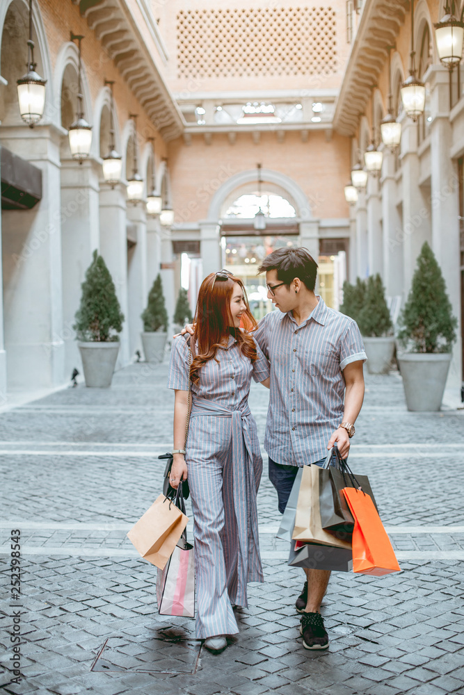 Asian couple walk shopping happily in the spacious department store. They have many shopping paper bags in hands.