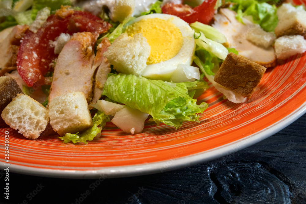 Caesar salad in red plate. Caesar salad consists of roasted chicken breast, iceberg lettuce, tomato. Popular dish of European cuisine and cuisines of other countries of world.