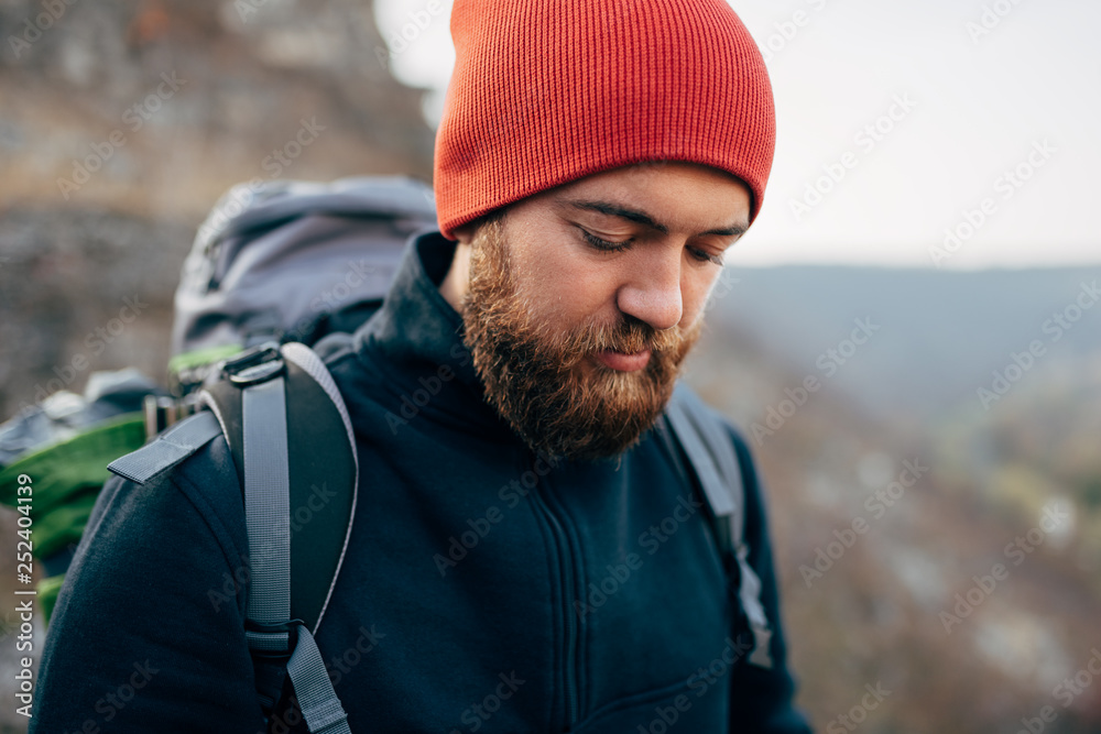 Closeup outdoors portrait of young handsome hiker male hiking in mountains wearing red hat. Traveler bearded man trekking and mountaineering. Travel, people and healthy lifestyle concept Closeup outdoors portrait of young handsome hiker male hiking in mountains wearing red hat. Traveler bearded man trekking and mountaineering. Travel, people and healthy lifestyle concept