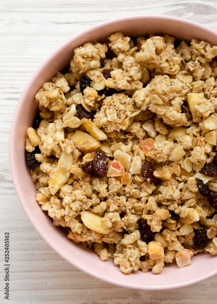 From above, pink bowl of fruit granola over white wooden surface. Top view, overhead, flat lay. From above, pink bowl of fruit granola over white wooden surface. Top view, overhead, flat lay.