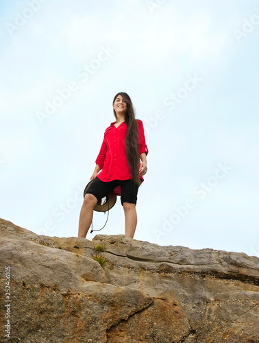 Teen girl in red shirt standing on high rock summit