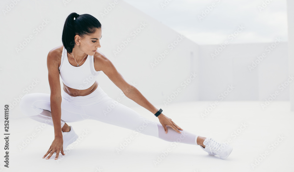 Woman in white fitness clothes doing warm up exercises - obrazy, fototapety, plakaty 