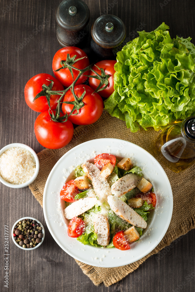 Fresh salad made of tomato, ruccola, chicken breast, eggs, arugula, crackers and spices. Caesar salad in a white, transparent bowl on wooden background