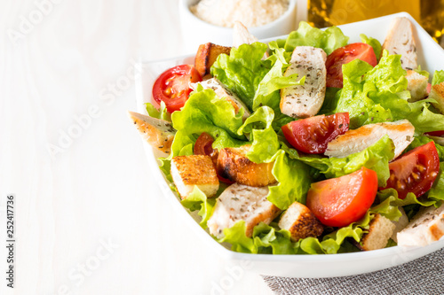 Fresh salad made of tomato, ruccola, chicken breast, eggs, arugula, crackers and spices. Caesar salad in a white, transparent bowl on wooden background