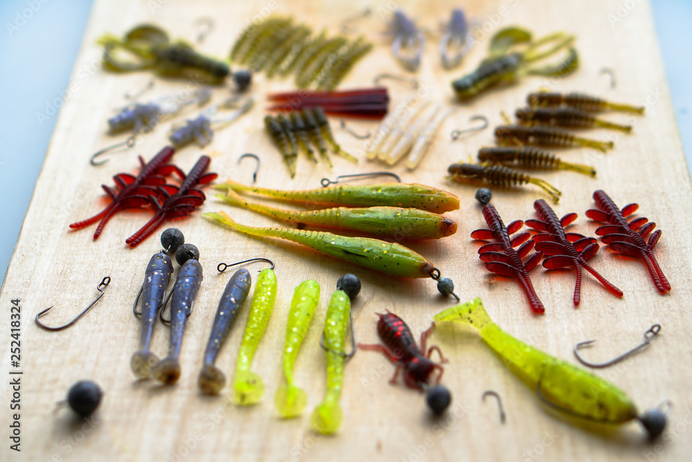 Colorful silicone fishing baits with plummets on wooden table. Various fish and worms and crayfish. Toned image and top view. Stock background, photo Colorful silicone fishing baits with plummets on wooden table. Various fish and worms and crayfish. Toned image and top view. Stock background, photo