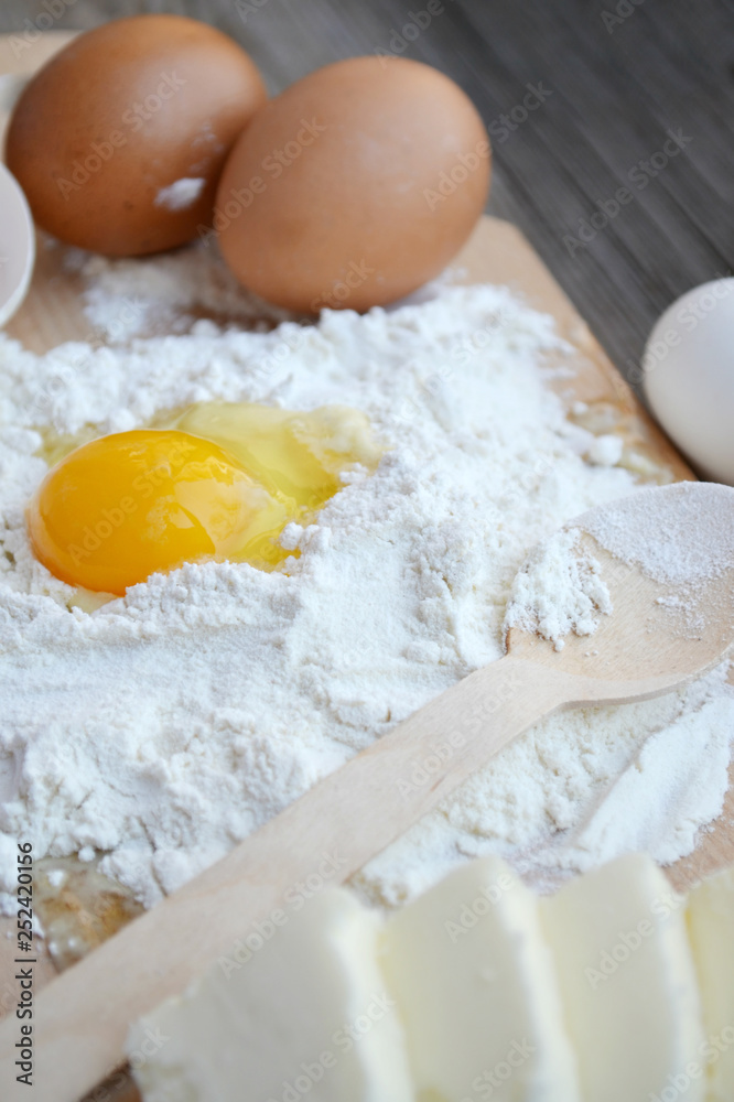 White flour with eggs, butter and wooden spoon on a cooking board White flour with eggs, butter and wooden spoon on a cooking board