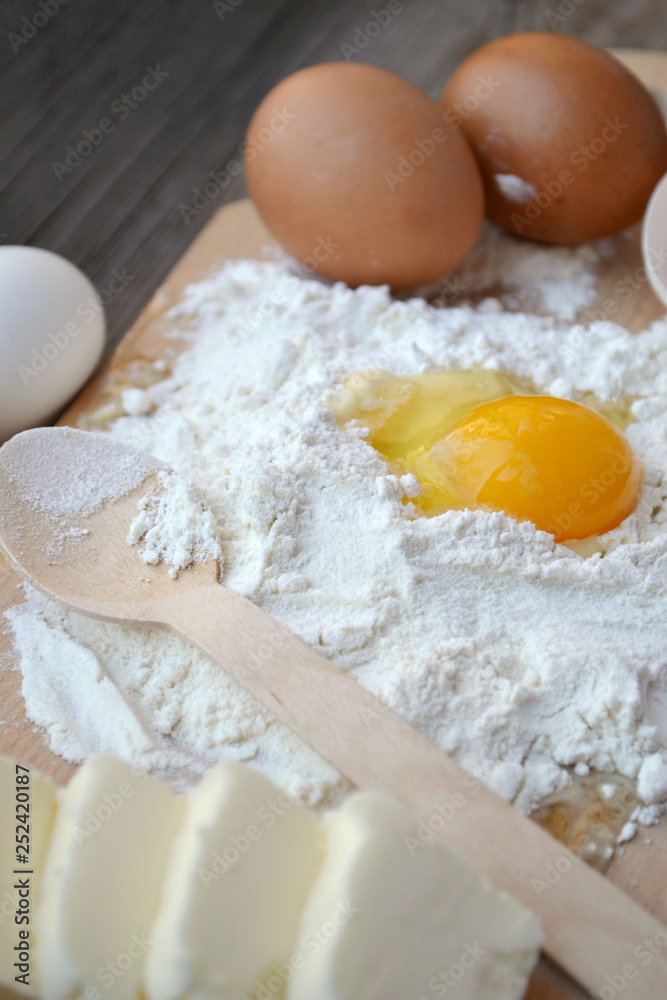 White flour with eggs, butter and wooden spoon on a cooking board White flour with eggs, butter and wooden spoon on a cooking board