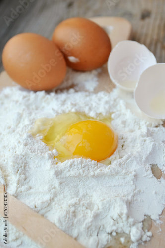 White flour with eggs, butter and wooden spoon on a cooking board