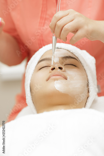 Attractive young Asian woman getting facial treatment at the spa salon