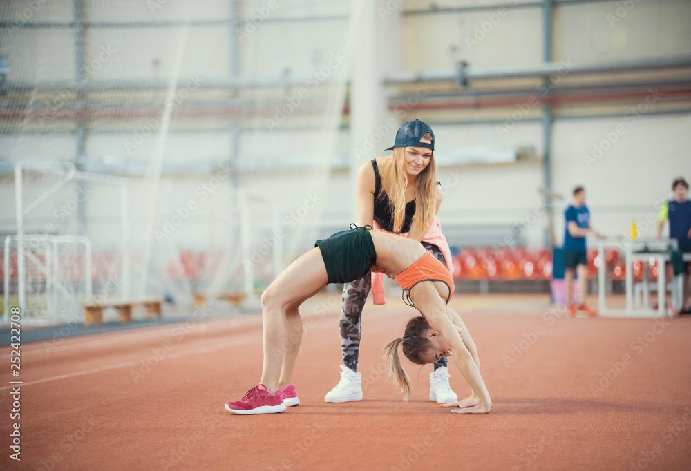 Two young women with blonde hair doing exercises and breathing hard in the sports hall together Two young women with blonde hair doing exercises and breathing hard in the sports hall together