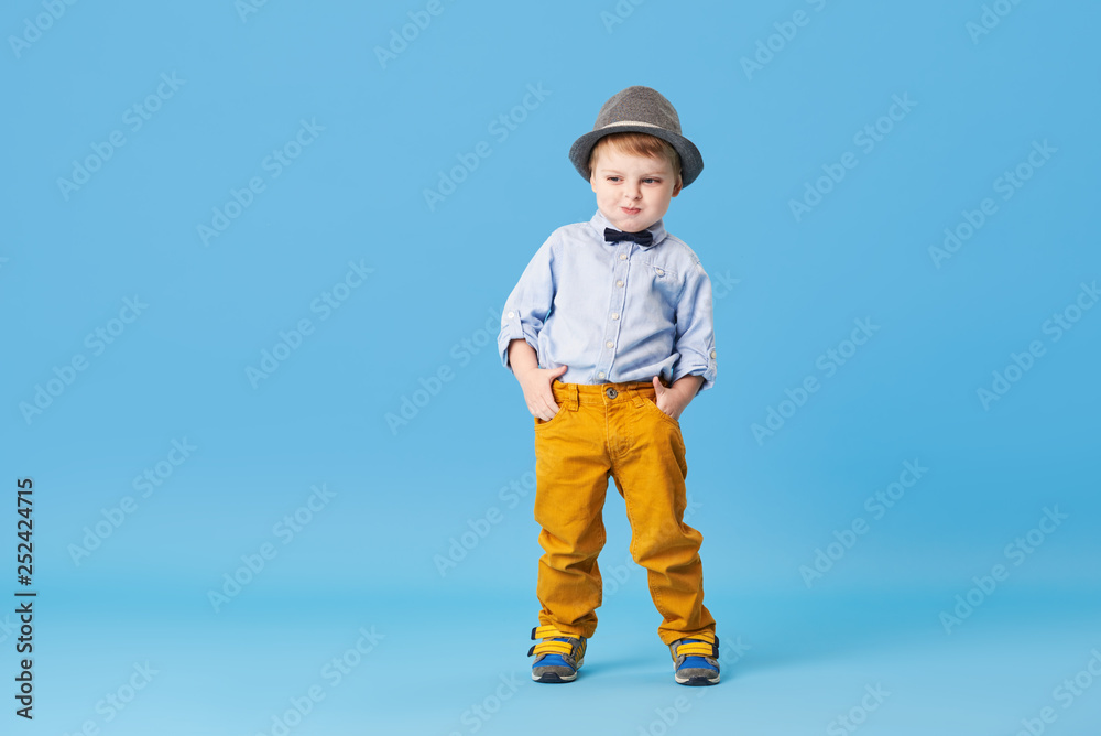 Portrait of happy joyful little boy isolated on blue background. Toddler child in hat and fashionable suit smiling and have a fun. Copy space for text left side Portrait of happy joyful little boy isolated on blue background. Toddler child in hat and fashionable suit smiling and have a fun. Copy space for text left side