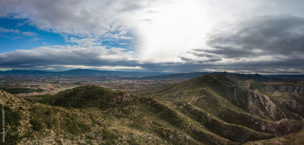 Panoramic view of mountains with dramatic sky and small town Canals, Spain in background.