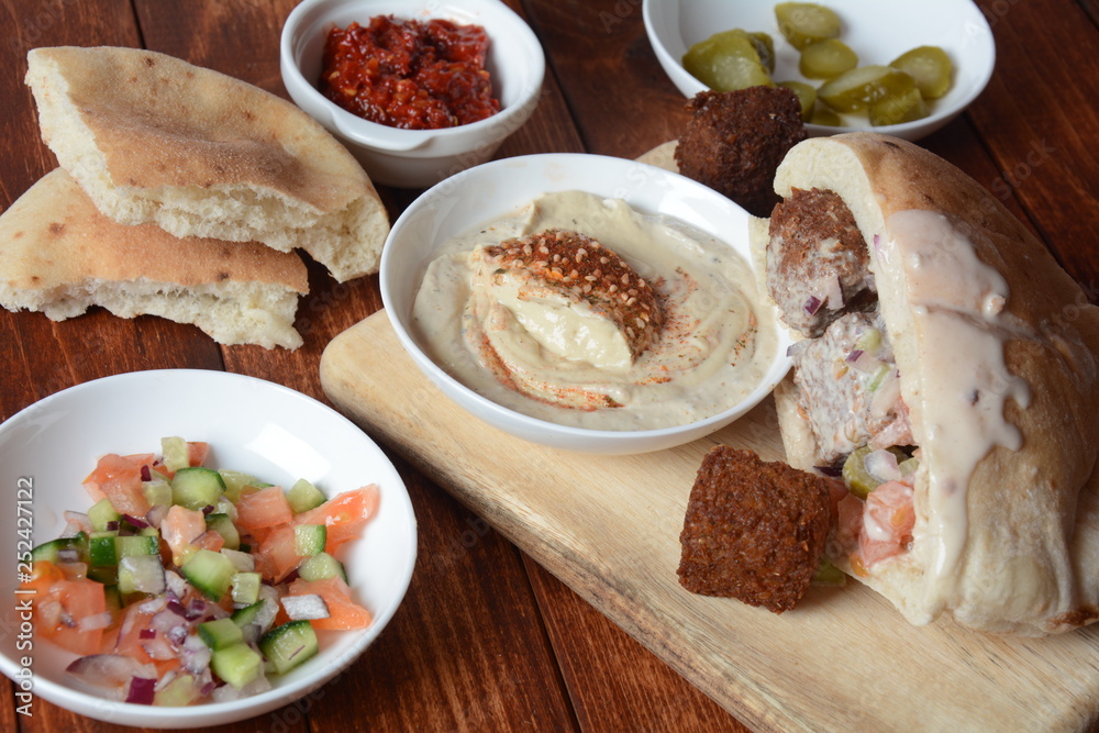 Falafel in pita bread with vegetable salad, harissa sauce, humus, tahini on wooden background. Traditional Israeli food. Middle eastern fast food concept Falafel in pita bread with vegetable salad, harissa sauce, humus, tahini on wooden background. Traditional Israeli food. Middle eastern fast food concept