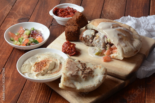 Falafel in pita bread with vegetable salad, harissa sauce, humus, tahini on wooden background. Traditional Israeli food. Middle eastern fast food concept