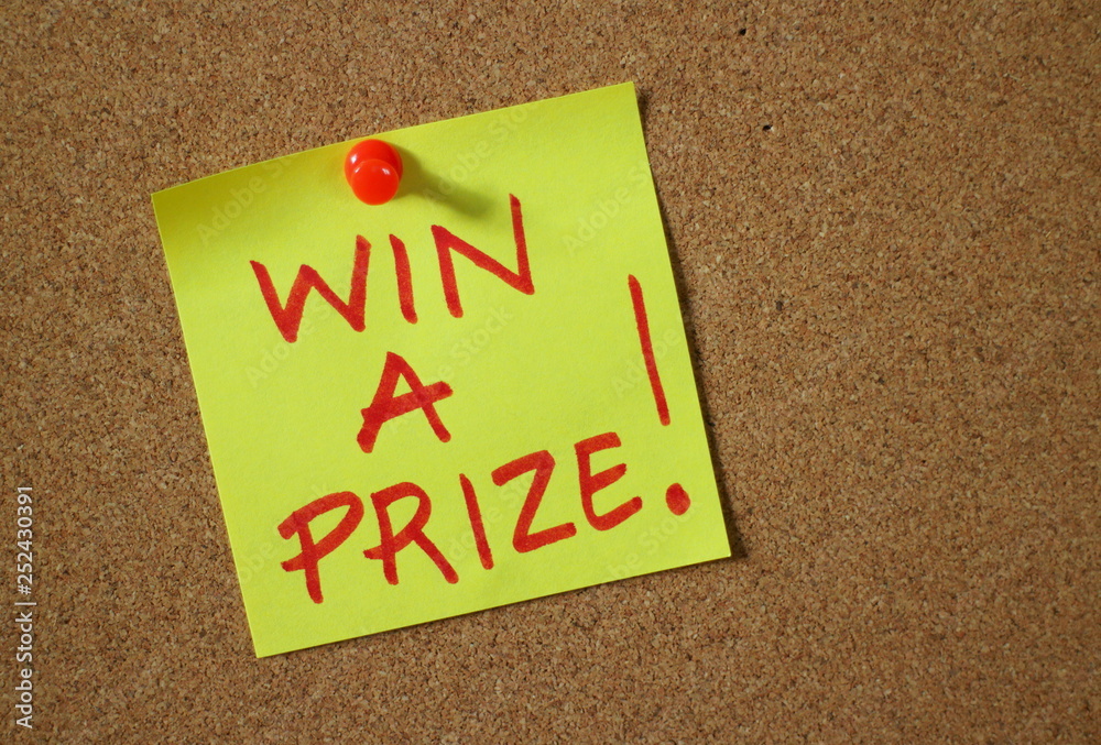 The words Win A Prize written by hand in red ink on a yellow sticky note pinned to a cork notice board as an incentive The words Win A Prize written by hand in red ink on a yellow sticky note pinned to a cork notice board as an incentive