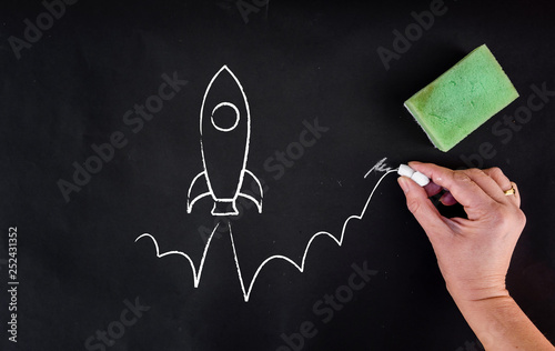 woman hand draws rocket launch on blackboard. Startup or boost concept