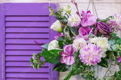 Garden design and decor to decorate the exterior of the facade of the house. A bouquet of different colors of purple hanging in a pot on the wall by the window.