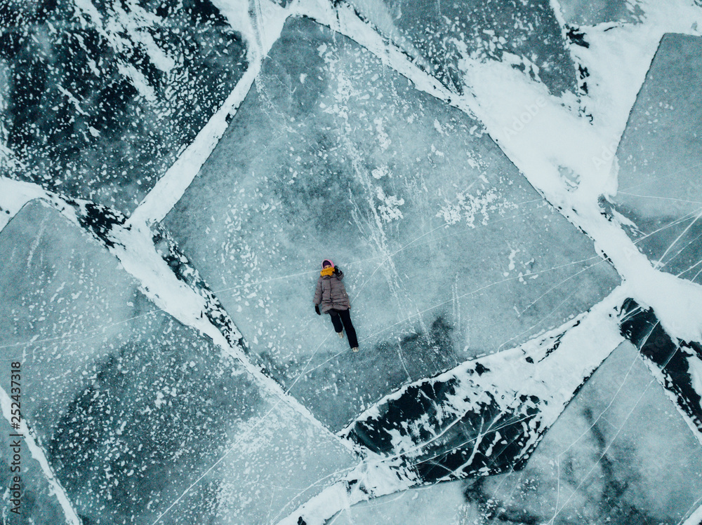 Naklejka premium Girl walking on the ice of lake Baikal. The whole surface of the ice is cracked. Ice just got up.