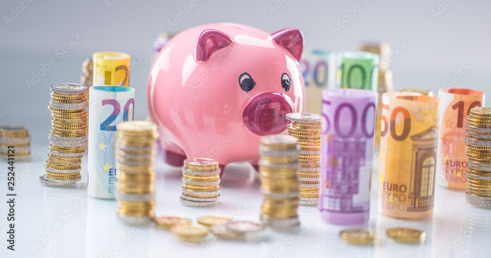 Pink piggy bank in the middle of rolled euro banknotes and towers with ...