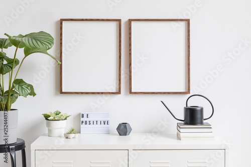 Minimalistic home decor of interior with two brown wooden mock up photo frames on the white shelf with books, black watering can tropical plants, box and home accessories. White walls. Mockup concept. © FollowTheFlow