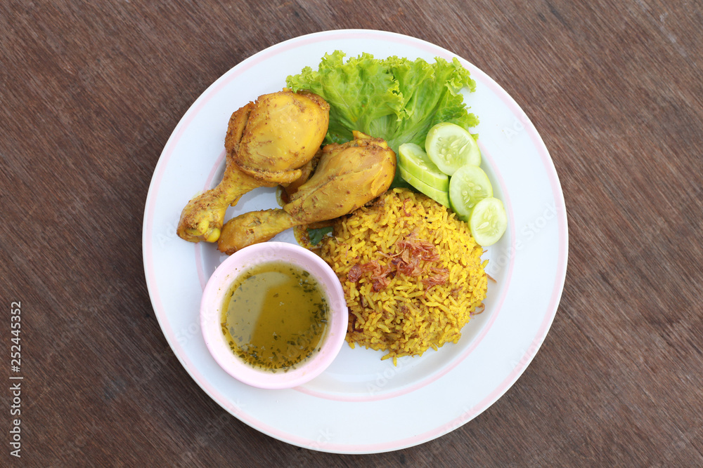 Muslim yellow rice with chicken in a white plate on a wooden floor Muslim yellow rice with chicken in a white plate on a wooden floor