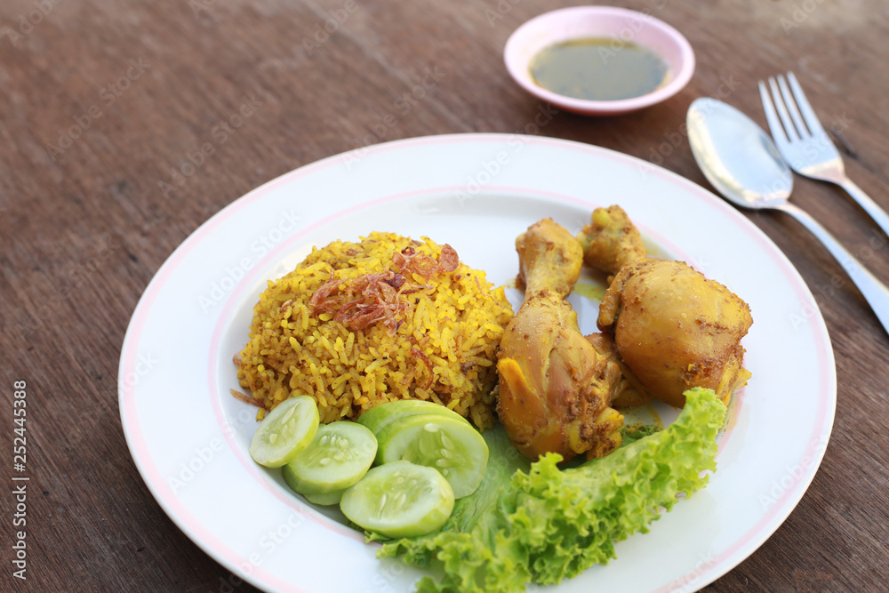 Muslim yellow rice with chicken in a white plate on a wooden floor Muslim yellow rice with chicken in a white plate on a wooden floor
