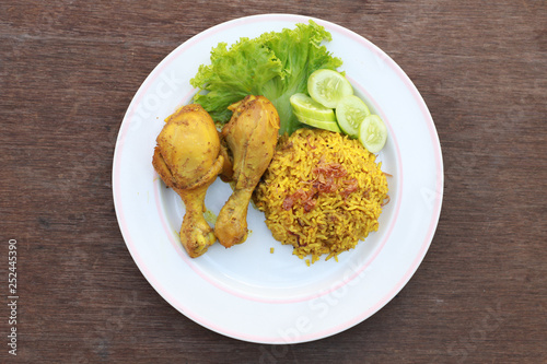 Muslim yellow rice with chicken in a white plate on a wooden floor
