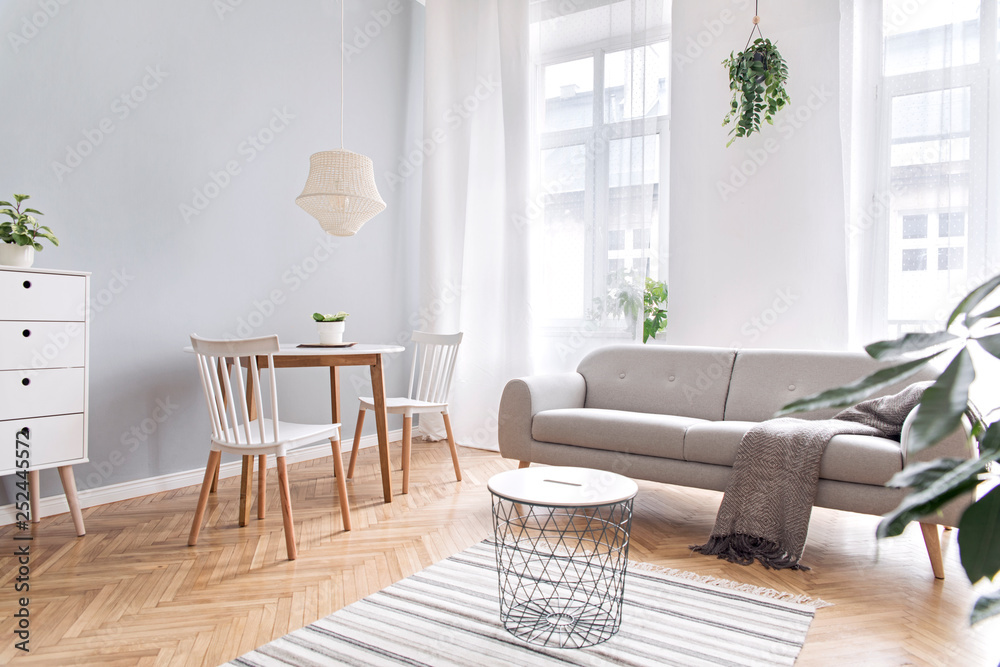 Modern scandinavian decor of living room with design furniture, family  table, sofa and plants Brown wooden parquet and stylish carpet. Nice and  minimalistic apartment. Big windows. Bright and sunny. foto de Stock