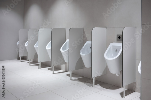 Line of white clean porcelain urinals in airport, cafe or restaurant. Public restroom for male users, minimalistic design. Typical arrangement of sensor-operated urinals in a row with partitions photo