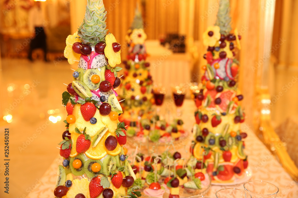 pyramid of fresh fruits and berries on a table with red wine and champagne
