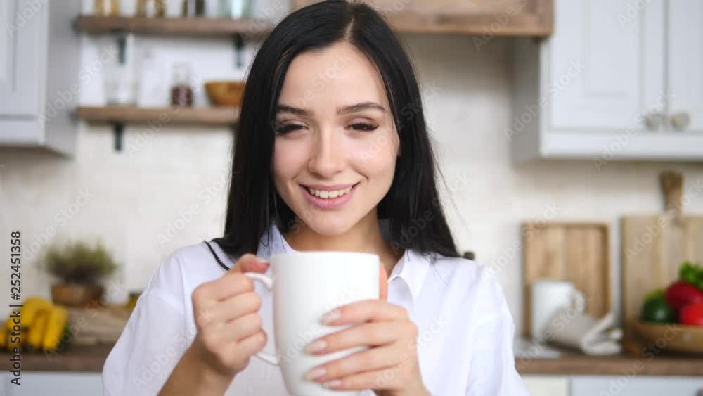 Portrait Of Attractive Brunette Female Looking At Camera Holding Cup In Kitchen