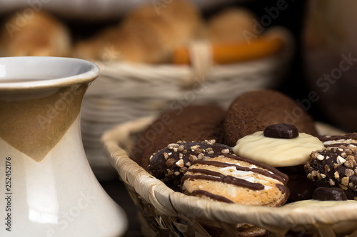 Cookies, in chocolate glaze, sprinkled with caramel crumbs and crushed nuts, lies in a wicker dish. Close-up.