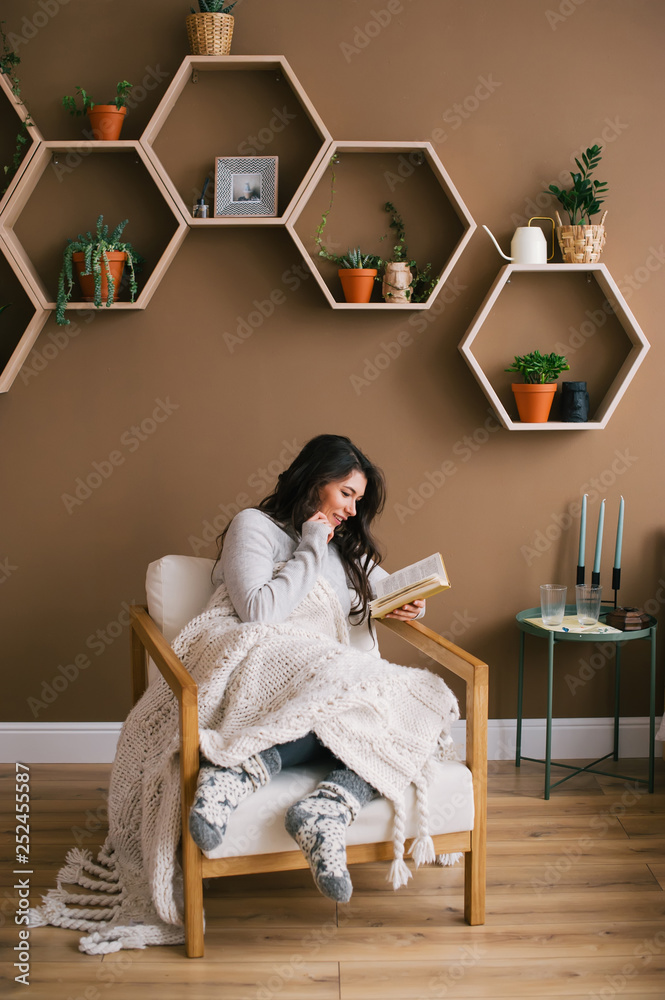Happy woman enjoying reading a book sitting on armchair in the home room