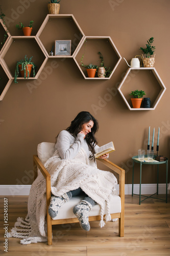 Obraz na płótnie Happy woman enjoying reading a book sitting on armchair in the home room w salonie