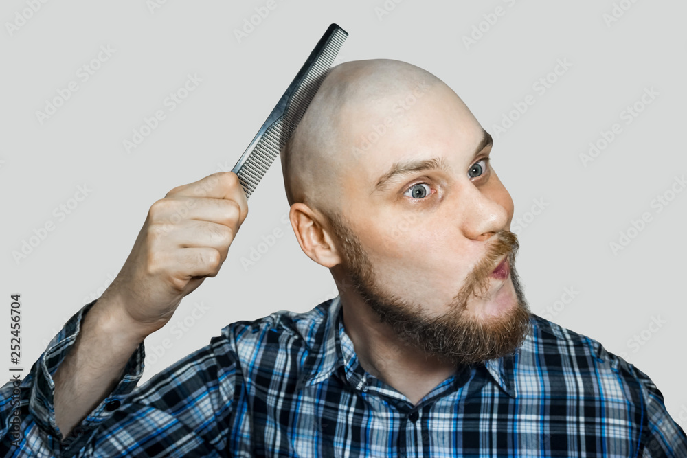 Bald funny guy with a beard and a comb in his hands, combing his head and  beard in the morning at home on a colored background. Concept: humor,  absurdity Stock Photo |