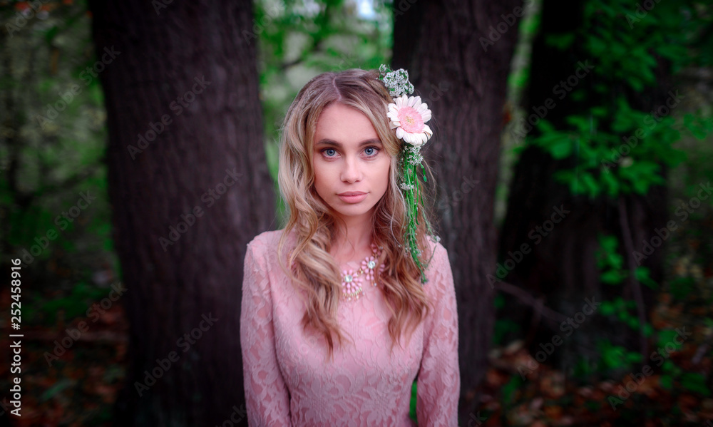 Naklejka premium beautiful woman with flowers in her blonde curls hair in laced pink dress posing in fairytale forest