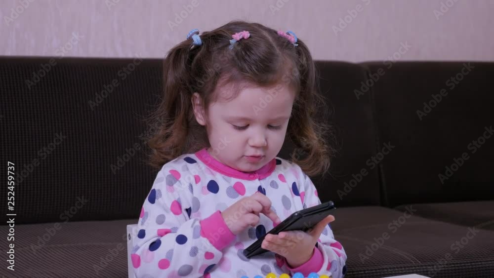 Little funny girl playing with phone at home.