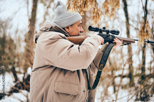 Senior man wearing stylish winter clothes walking with .22 scoped rifle in a forest on alert