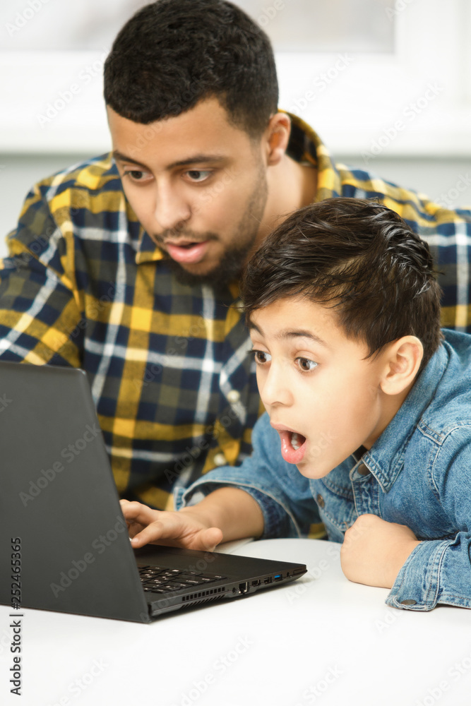 Cheerful young boy and his father using a laptop together