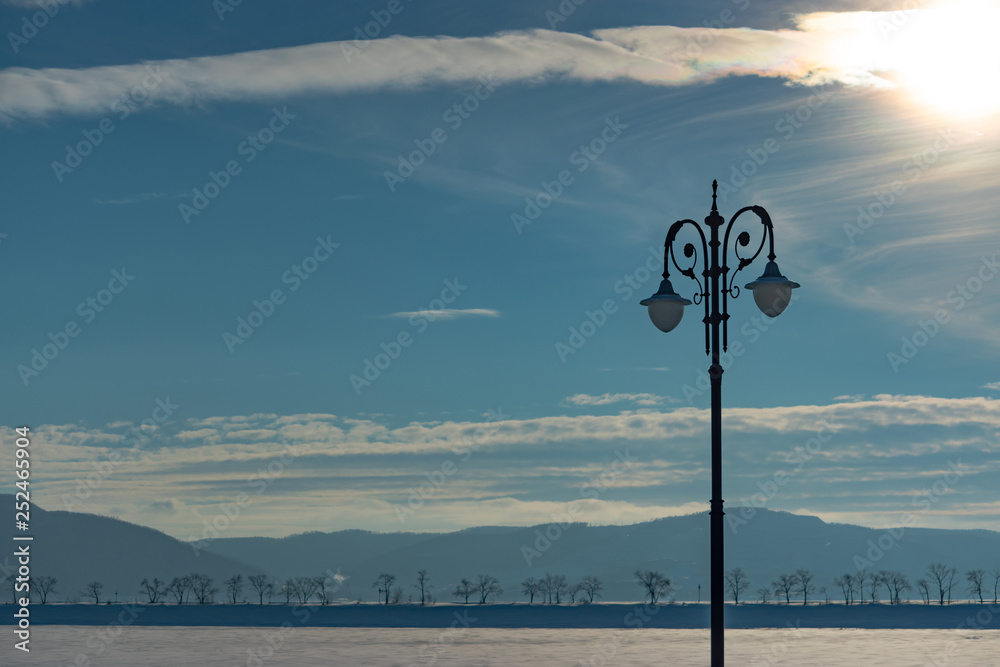 Winter view of the snow covered city on the river bank. Embankment with vintage metal lanterns