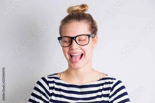 Crazy funny young blond woman in glasses showing tongue and smiling on white background