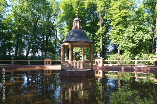 Small wooden house with scaffolding on the water in the garden pond, surrounded by trees 