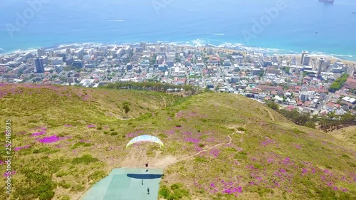 Drone aerial over paragliding and paragliders with the downtown city of Cape Town, South Africa, in background.